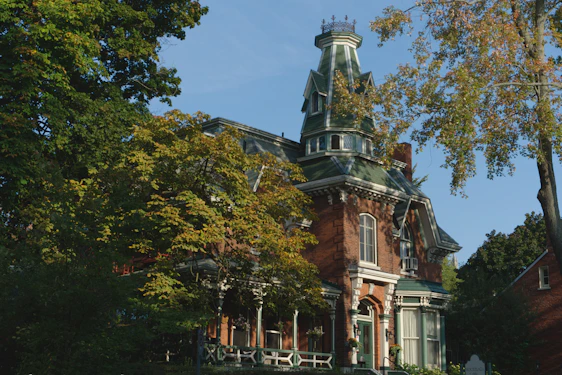 Victorian-era mansion exterior bathed in warm golden light at sunset, highlighting intricate architectural details and lush gardens.