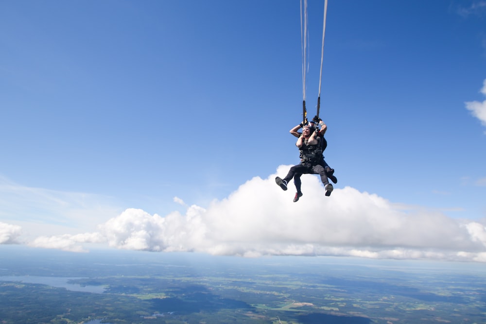 2 person in black jacket and black pants riding on black parachute under blue sky during