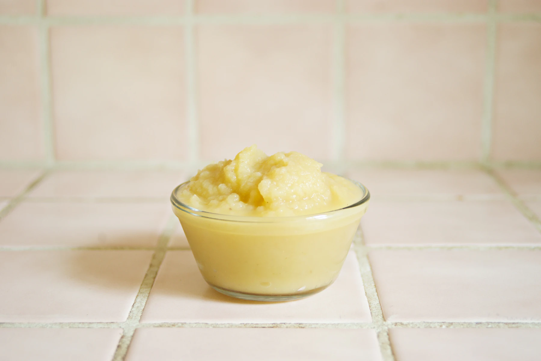 Smooth pale-yellow fruit puree in a small glass bowl on pink tile