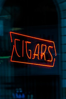 A bright red neon sign displays the word 'CIGARS' against a dark, reflective surface that appears to be a window.
