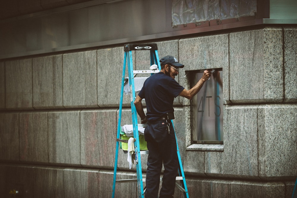 man in blue t-shirt and blue pants standing on ladder