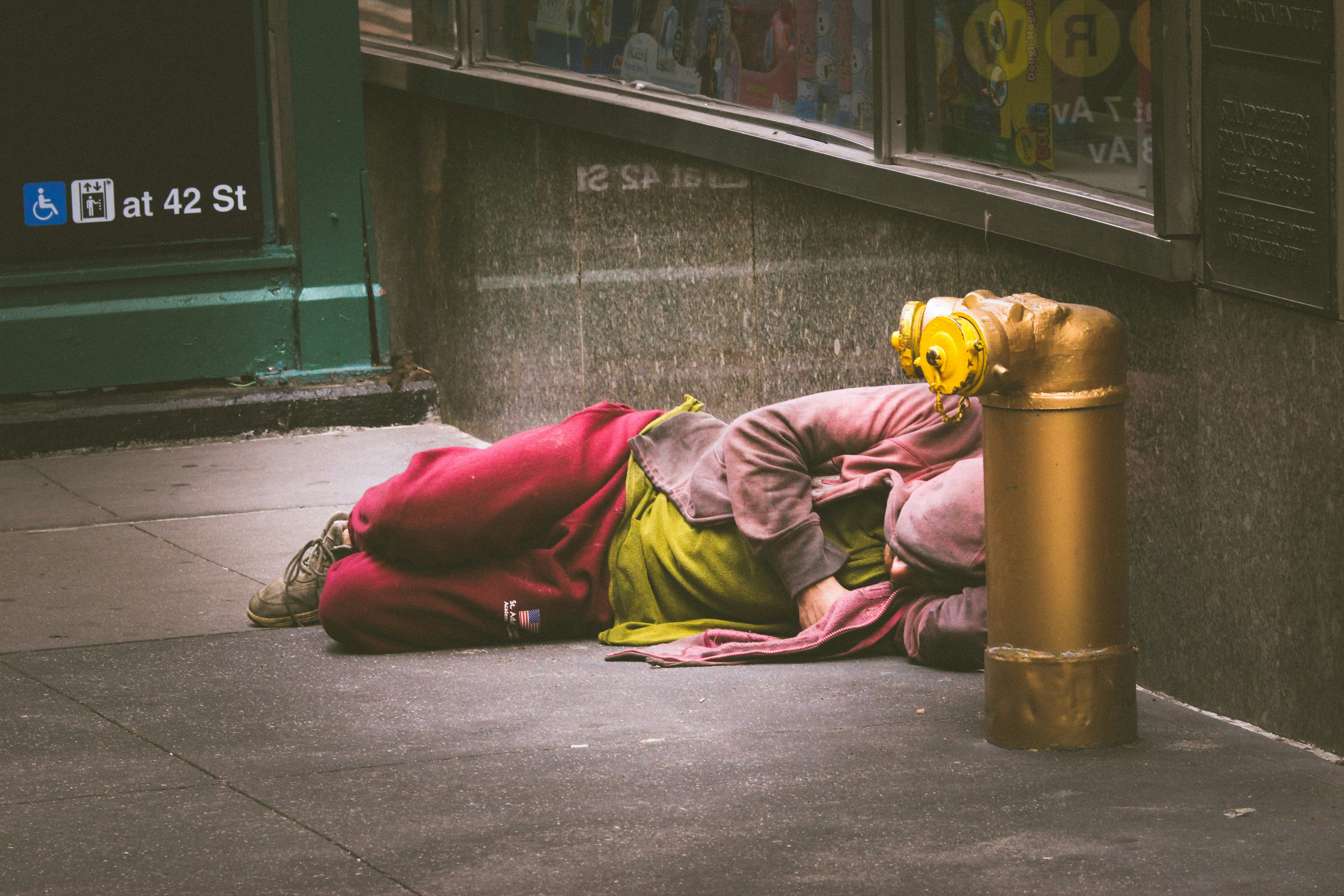 person in green and red long sleeve shirt and brown pants sitting on gray concrete floor