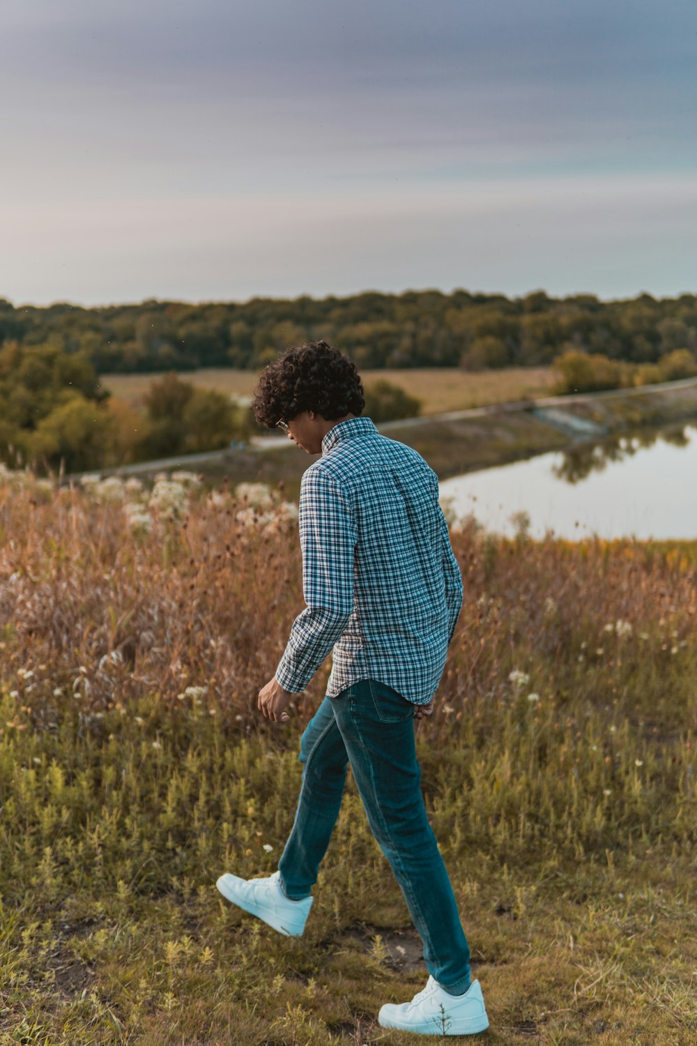 man in blue and white checkered dress shirt and blue denim jeans standing on green grass