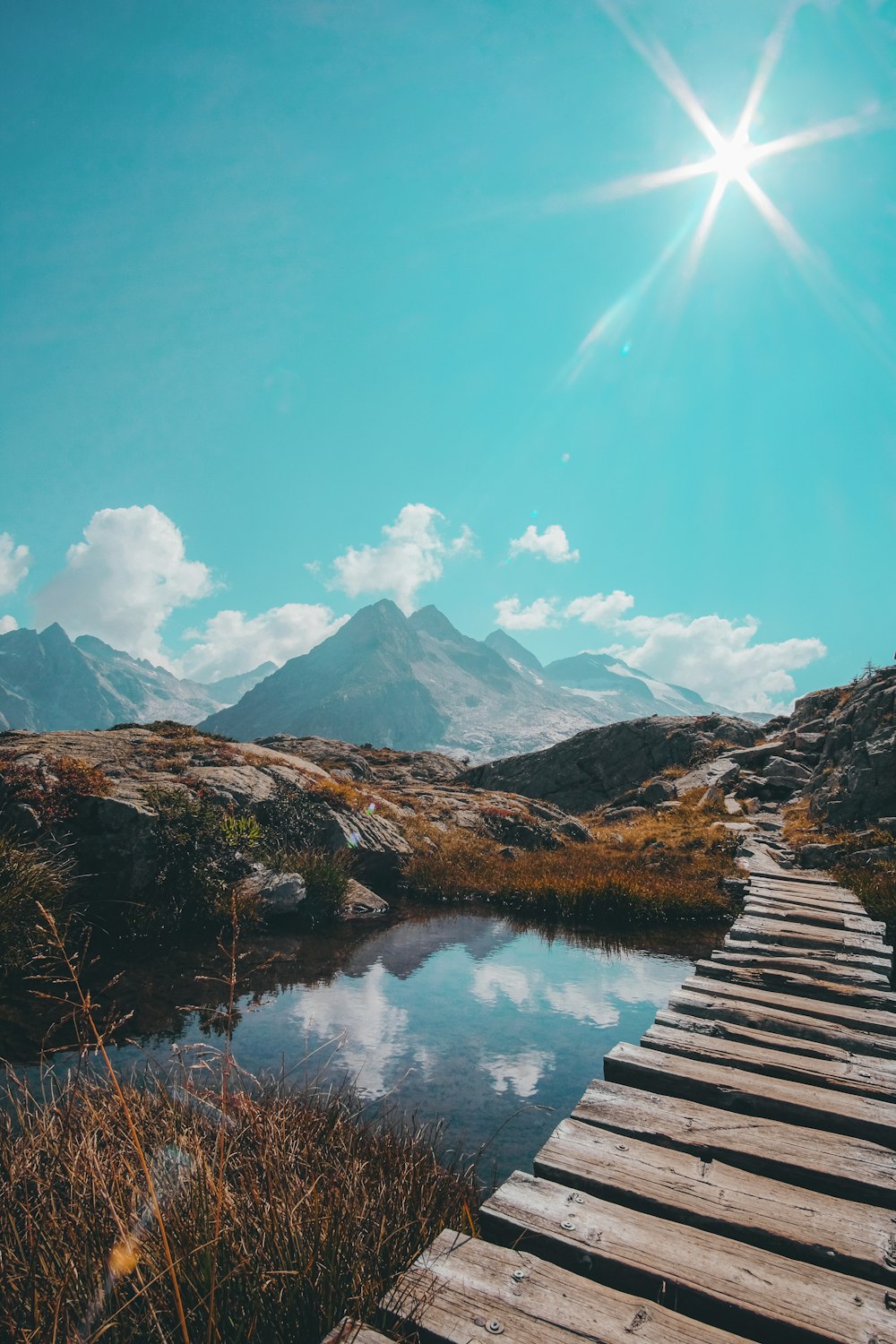 brown wooden dock on lake near mountains under blue sky during daytime