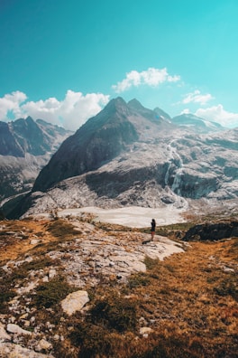 Hiker standing on a rocky peak overlooking a vast Italian mountain range under clear blue skies.