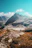 A smiling hiker standing on a rocky peak overlooking the lush, rugged Prokletije mountains under a clear blue sky.