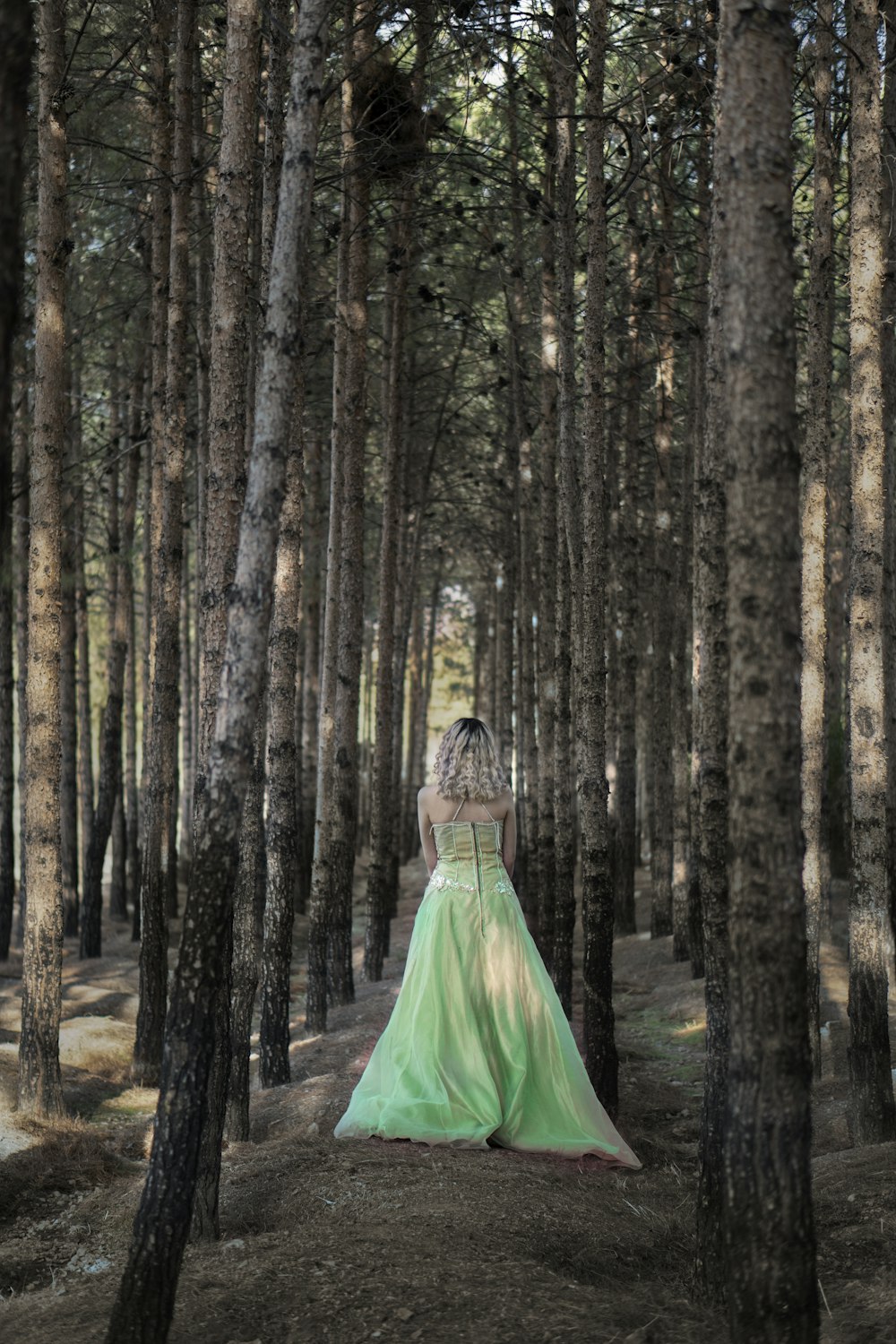 woman in green dress standing in the middle of the forest