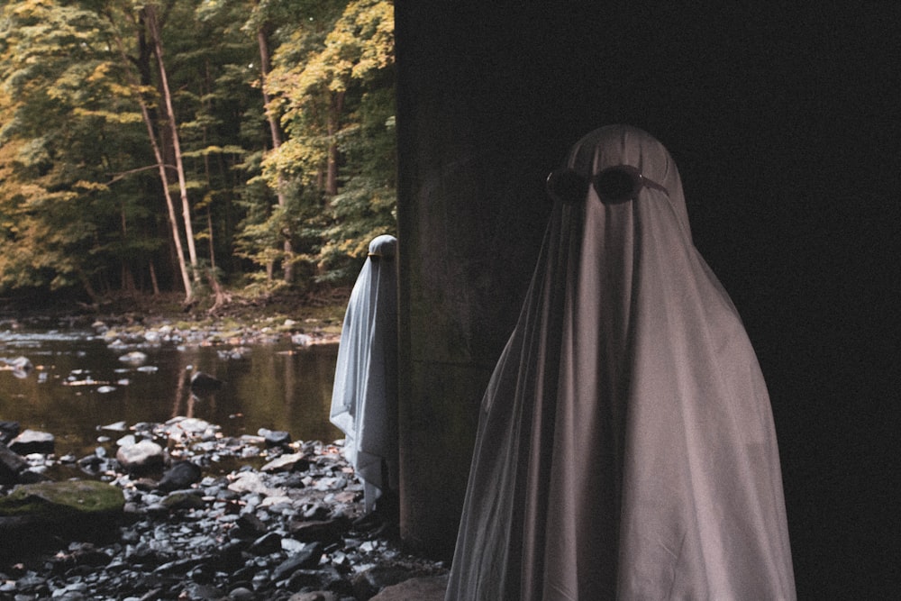 person covered with white textile standing on rocky ground near river during daytime