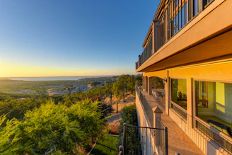 Elegant flat balcony overlooking calm blue waters surrounded by lush greenery during sunset.
