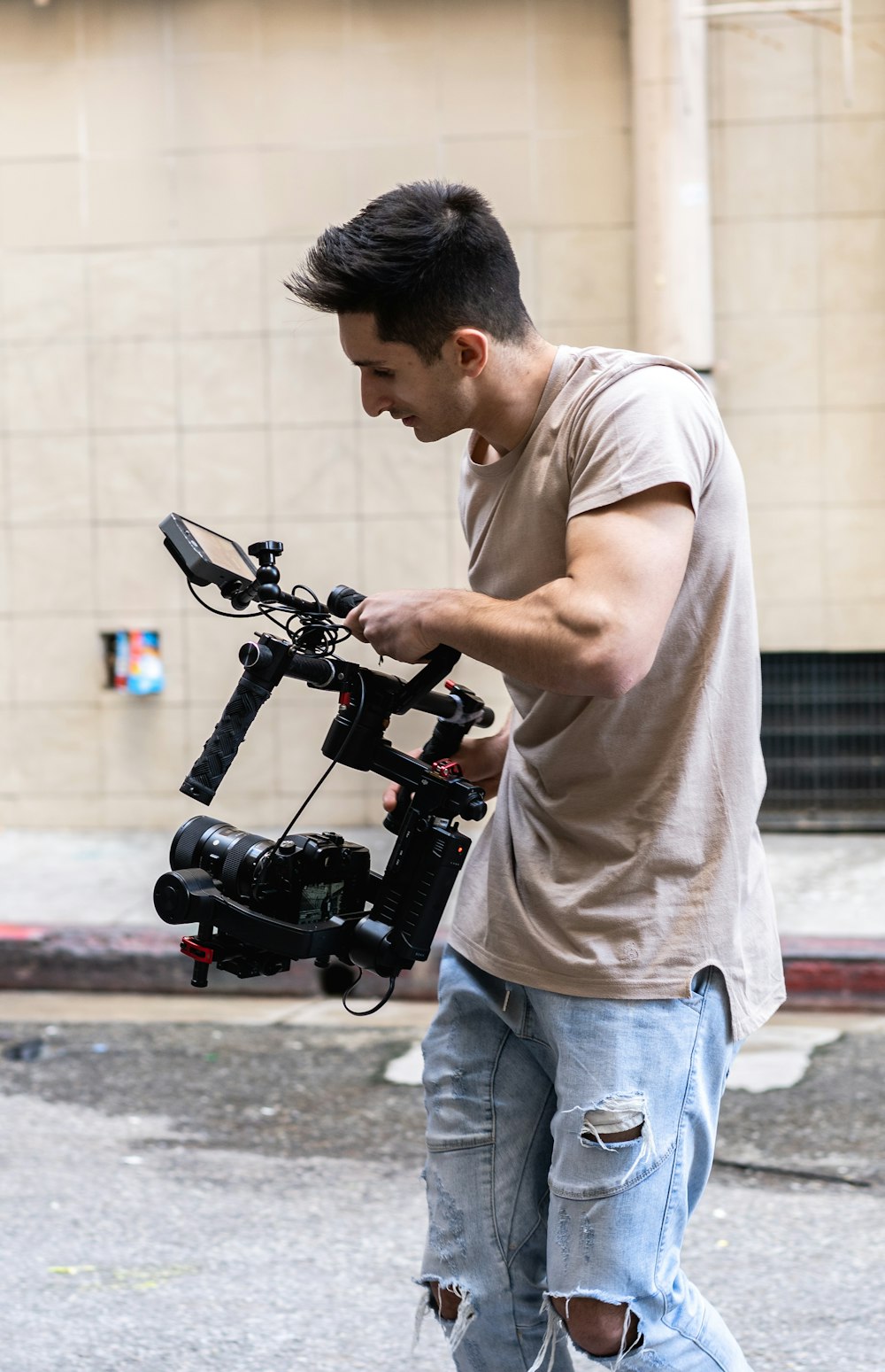 man in white t-shirt and blue denim jeans holding black video camera