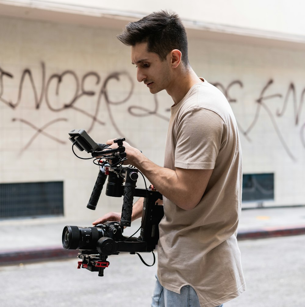 man in white t-shirt and gray pants holding black video camera