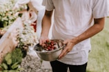 person in white t-shirt holding red round fruits