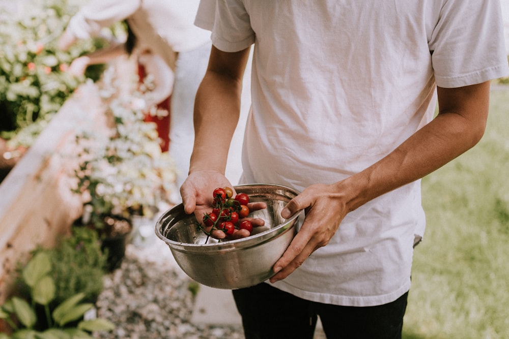 person in white t-shirt holding red round fruits