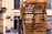 A large stack of wooden pallets is piled up on the side of a street next to a building with arched windows. The scene appears to be set in an urban environment with some bicycles visible in the background.