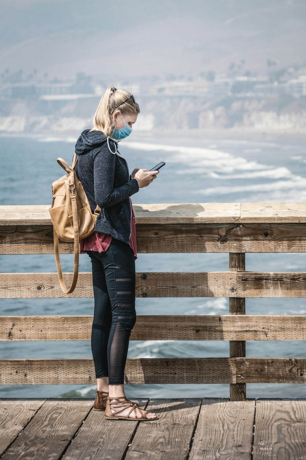 woman in blue denim jacket and black pants standing on brown wooden fence during daytime