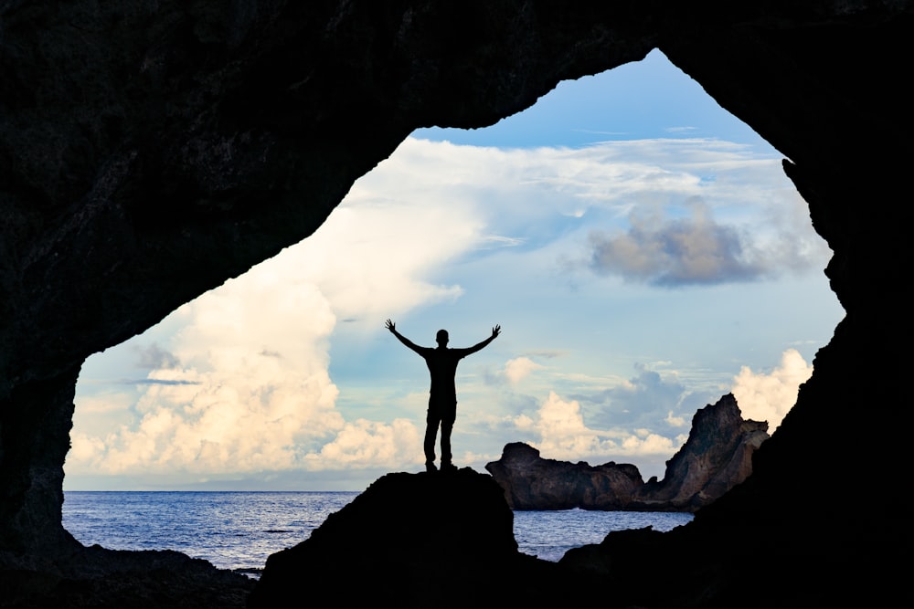 silhouette d’homme debout sur la formation rocheuse pendant la journée