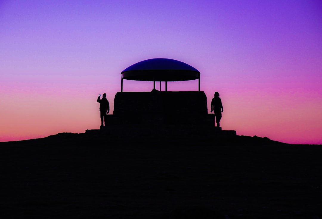 silhouette of people sitting on chair under blue umbrella during sunset