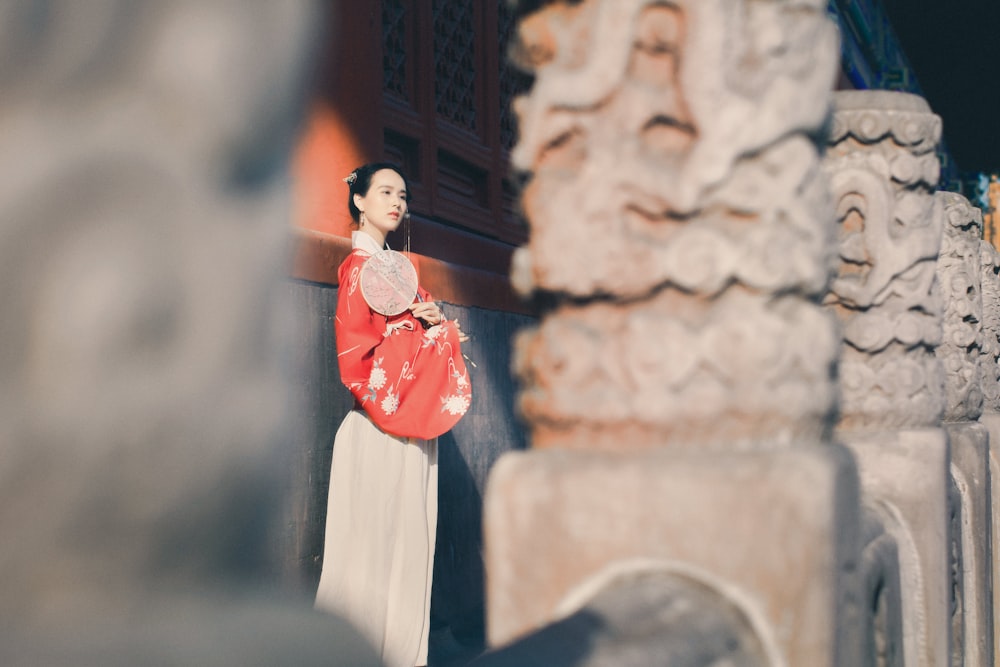 Mujer con vestido rojo de manga larga de pie cerca de una pared de concreto marrón durante el día