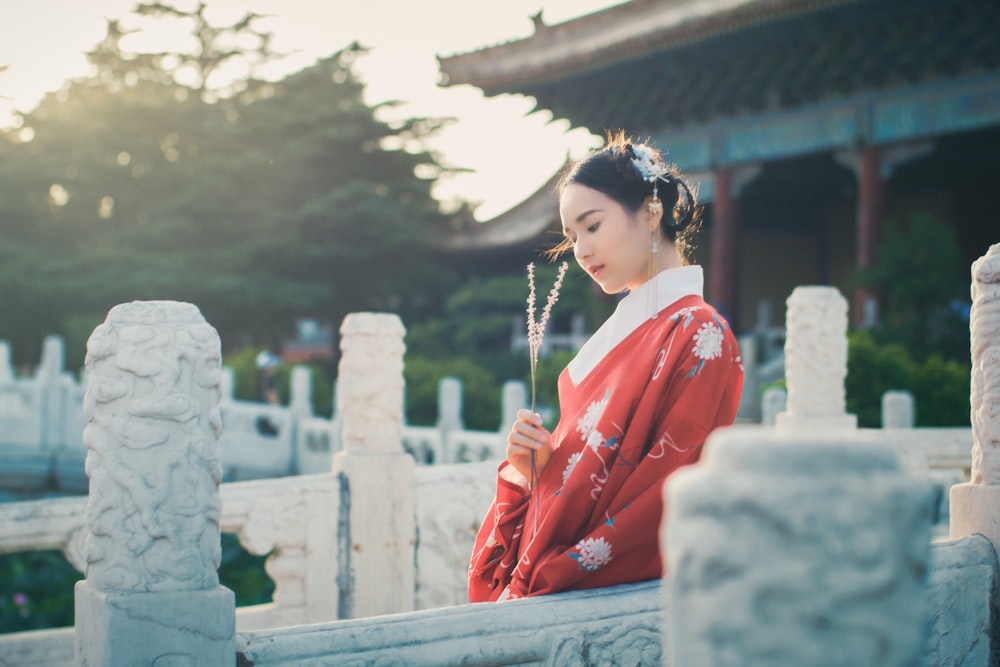 woman in red robe sitting on gray concrete bench during daytime