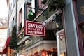 A storefront featuring a prominent red and white sign that reads 'Swiss Quality Souvenirs.' The shop is adorned with festive decorations, including green garlands and a shiny green ornament. Windows display various items inside, hinting at a welcoming shopping environment. Traditional Swiss symbols and colors are prominently showcased.