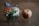 A fresh salad in a clear plastic container, featuring ingredients like shredded carrots, lettuce, cheese cubes, sliced egg, and deli meat. Next to it is an apple, light red with a hint of yellow, resting on a flat surface.