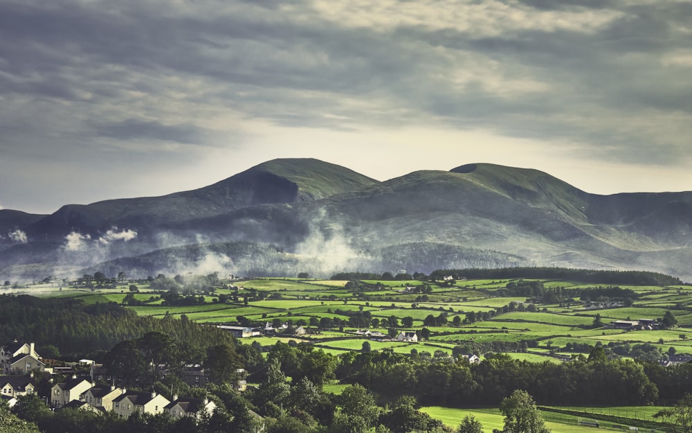 green grass field near mountain under white clouds during daytime