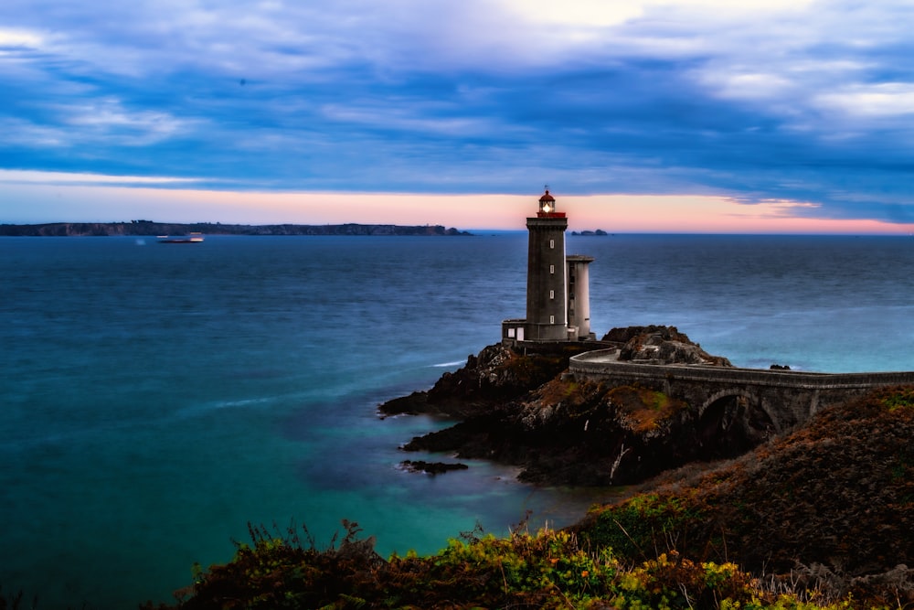 日没時の水域近くの茶色の岩層の白い灯台