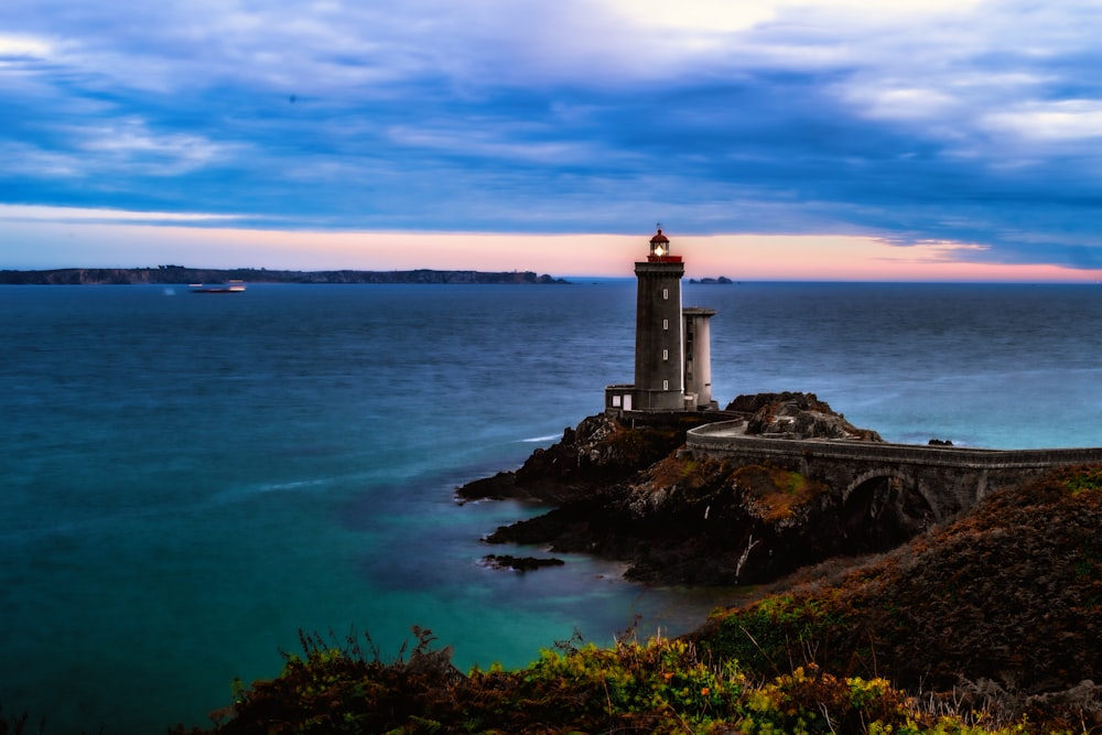 white lighthouse on brown rock formation near body of water during sunset