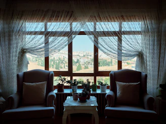 A cozy sitting area with cream-colored armchairs and a large window overlooking the city