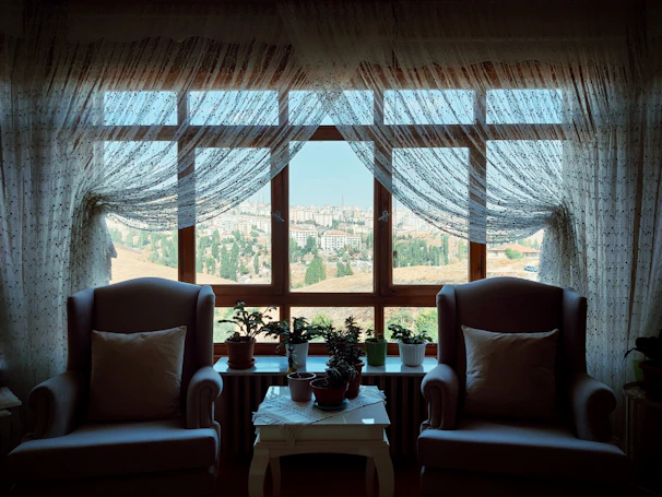 A cozy sitting area with cream-colored armchairs and a large window overlooking the city