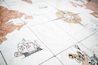 An illustrated map on stone or tiles depicting a sailing ship with red cross symbols, a mythical figure blowing a horn, and a compass rose. The map features landmasses outlined in brown and beige with various maritime symbols.