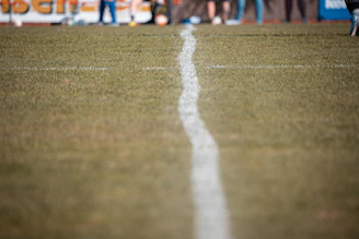 Close-up of a football on the grass field with a blurred scoreboard in the background.