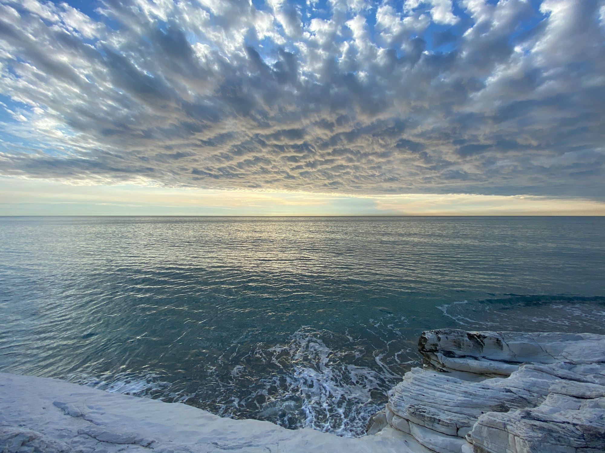 ocean waves crashing on rocks under blue and white cloudy sky during daytime