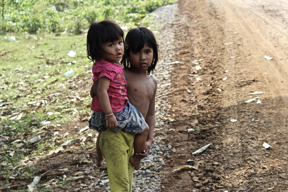 girl in pink tank top and green pants sitting on brown soil during daytime