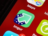 A close-up of a smartphone screen displaying various app icons including Imgur and Maps. The Imgur icon is green with an upward arrow and star pattern.