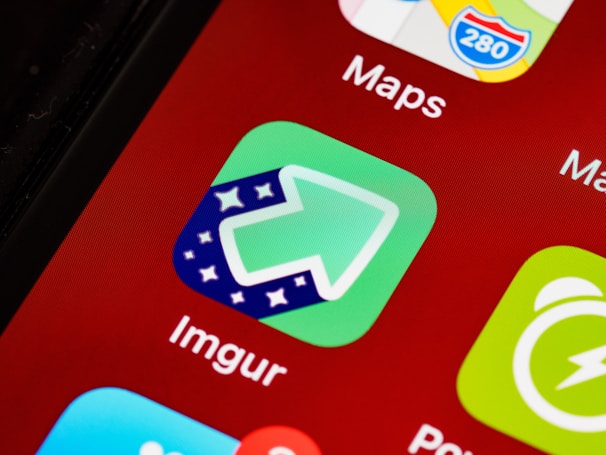 A close-up of a smartphone screen displaying various app icons including Imgur and Maps. The Imgur icon is green with an upward arrow and star pattern.