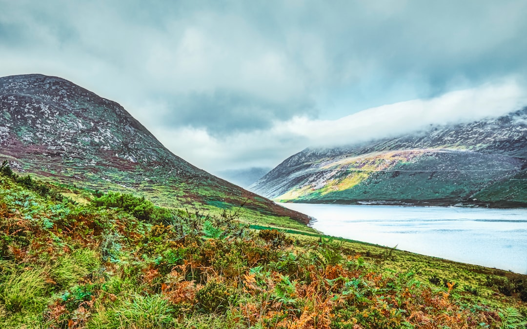 green and brown mountain beside body of water under cloudy sky during daytime