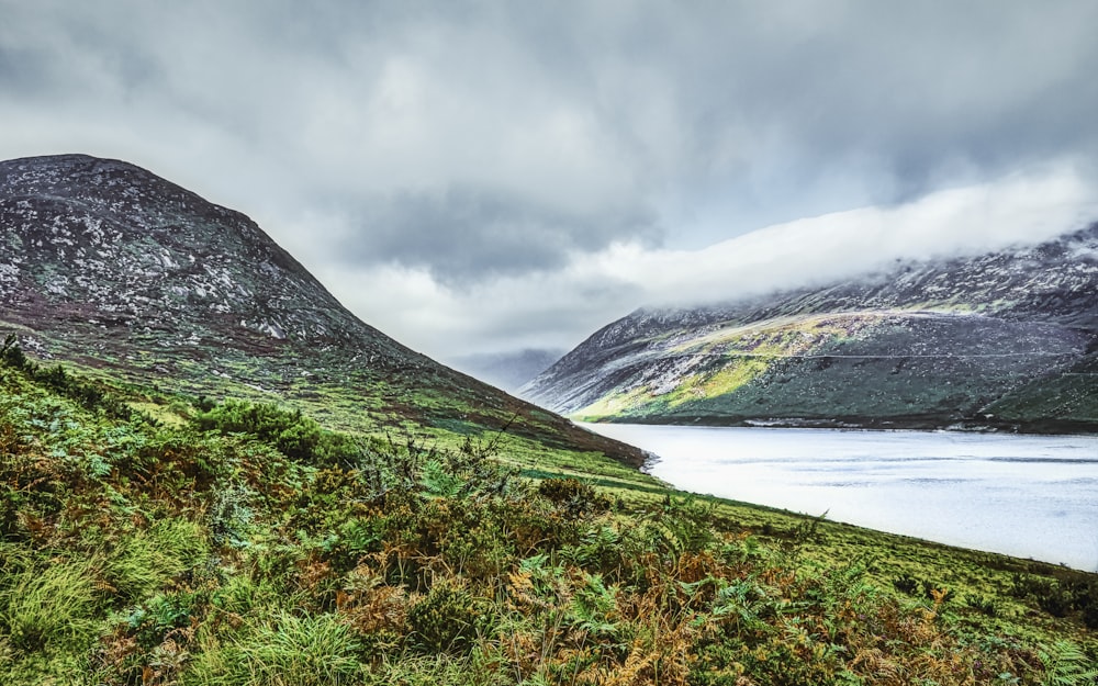 green and brown mountain beside body of water under cloudy sky during daytime