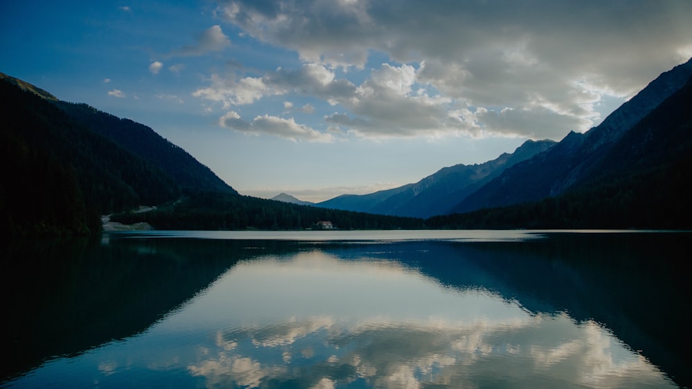 lake near mountain under white clouds and blue sky during daytime