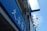 A blue outdoor sign with white text, featuring Asian characters and the word 'PHARMACY'. It's mounted on a building facade, surrounded by other signs and what appears to be an air conditioning unit.