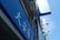 A blue outdoor sign with white text, featuring Asian characters and the word 'PHARMACY'. It's mounted on a building facade, surrounded by other signs and what appears to be an air conditioning unit.