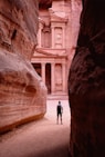 person walking on pathway between brown rock formation during daytime