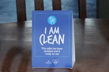 A blue table sign displays the text 'I AM CLEAN' with additional smaller text stating 'This table has been sanitised and is ready to use.' The sign includes a circular logo at the top depicting a hand with bubbles.
