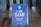 A blue table sign displays the text 'I AM CLEAN' with additional smaller text stating 'This table has been sanitised and is ready to use.' The sign includes a circular logo at the top depicting a hand with bubbles.