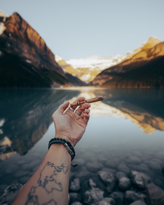 person holding cigarette stick near lake during daytime in Banff National Park Canada