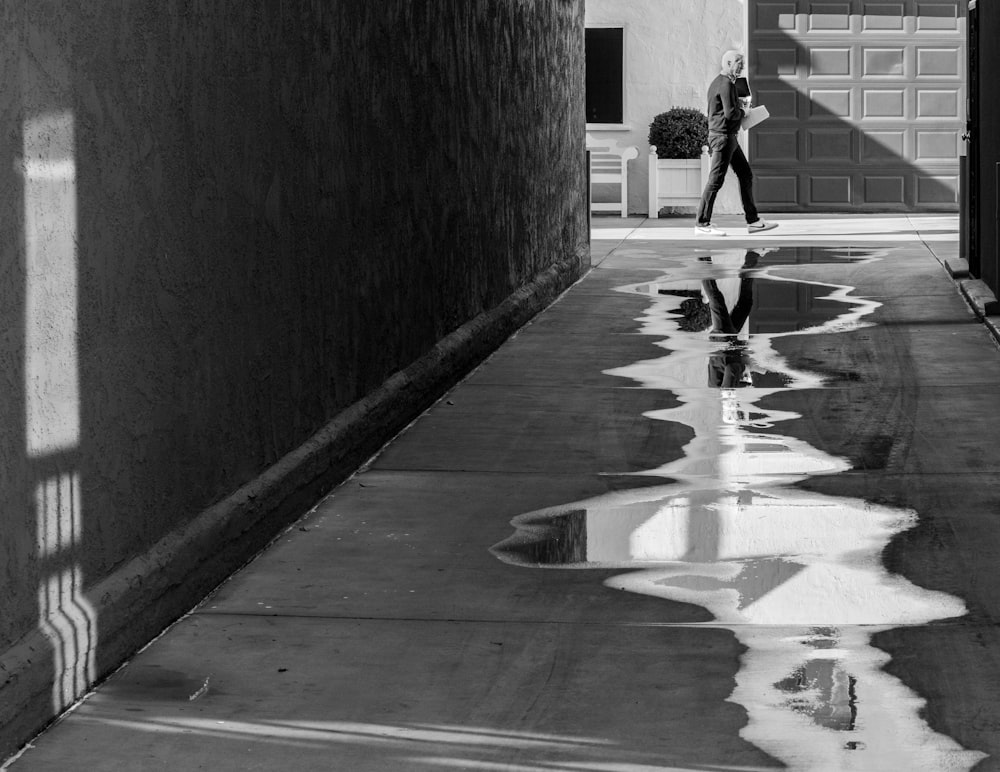 grayscale photo of woman walking on sidewalk