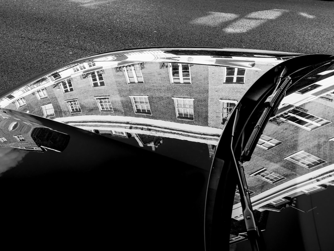 grayscale photo of car on road, Traditional London buildings reflected in the hood and windshield of a car.