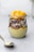 Close-up of a creamy pudding in a glass jar with caramel topping and a delicate spoon beside it.