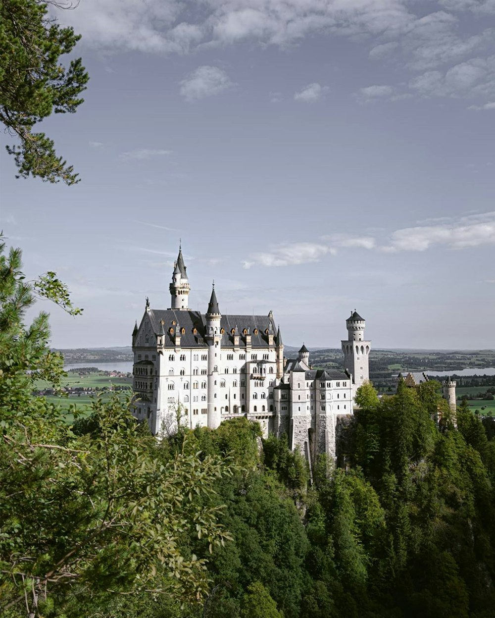 white and black castle near green trees under white clouds and blue sky during daytime