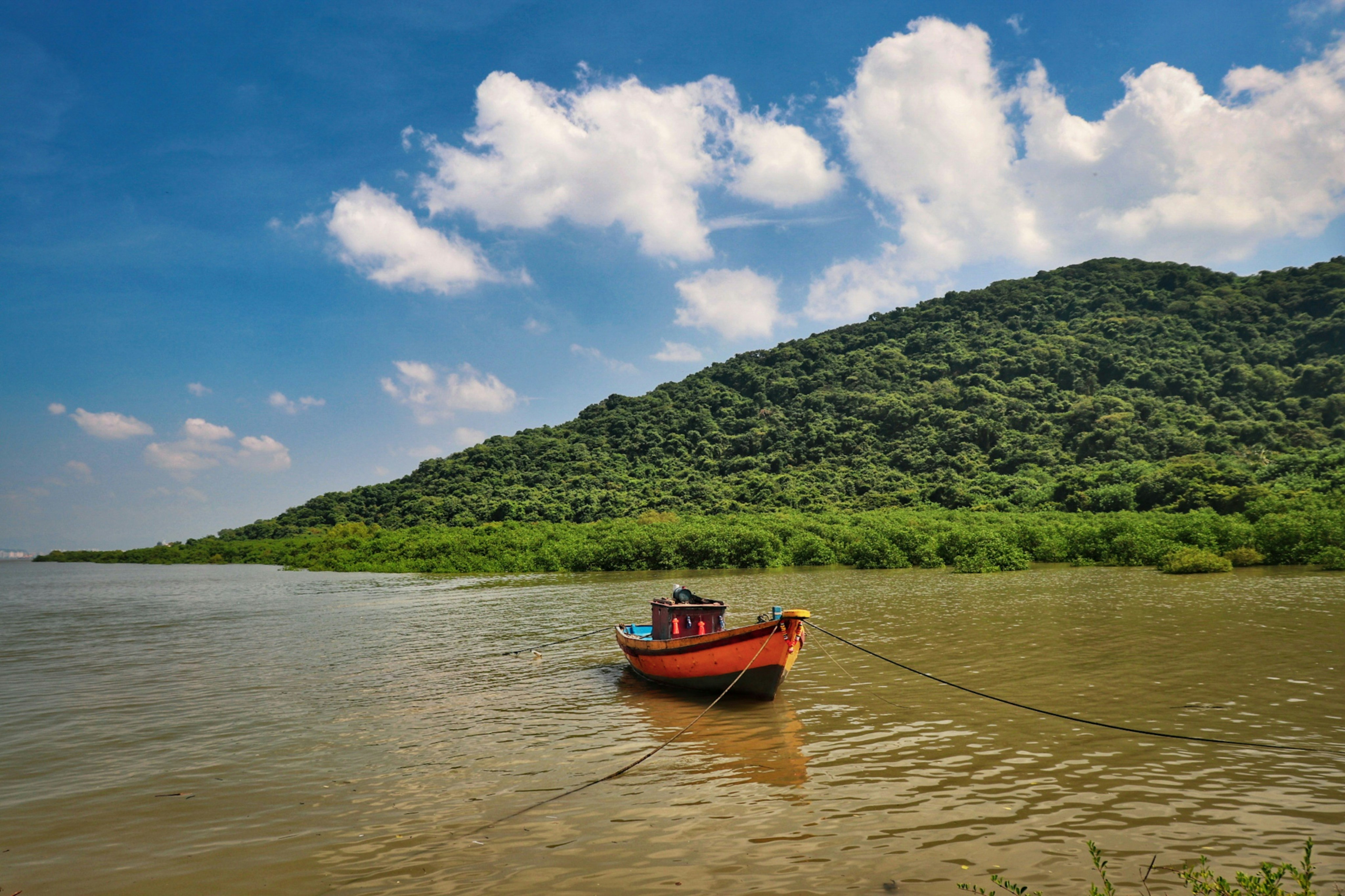 red boat on body of water near green mountain under blue and white sunny cloudy sky